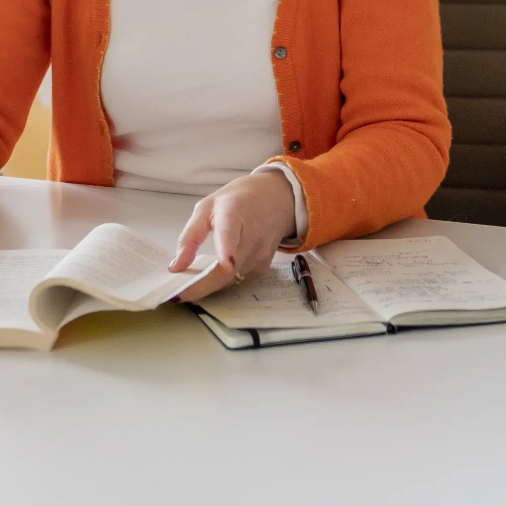 Eine Hand, die in einem Buch blättert, das dauf einem Notizbuch liegt als Symbol für den Workshop "Schreiberei – der ultimative biografische Schreib-Workshop für Frauen Ü45".